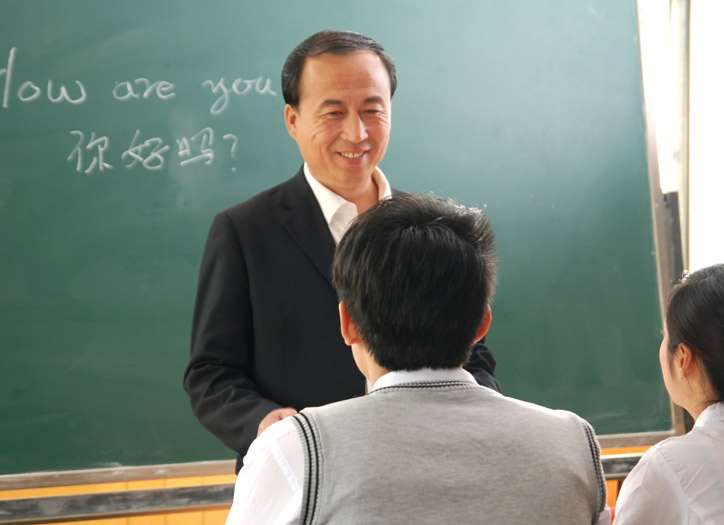 Chinesischkurs in einer kleinen Gruppe. Der Lehrer steht vor den Teilnehmenden und hört diesen lächelnd zu.