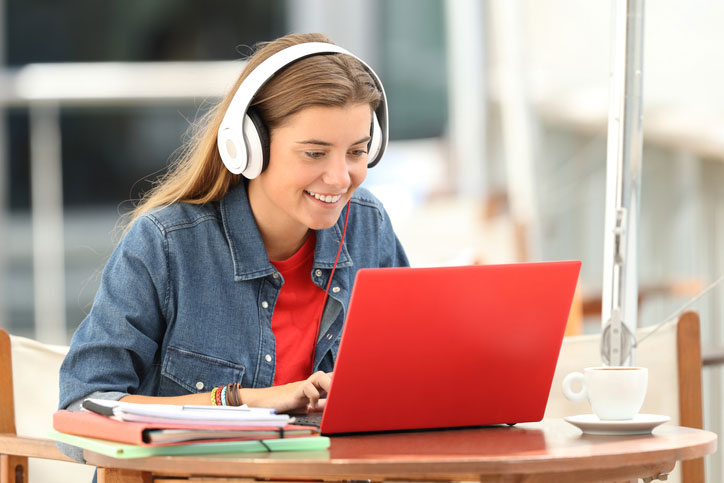Eine junge glückliche Frau mit Kopfhörer lernt Englisch online per e-Learning auf ihrem Laptop.